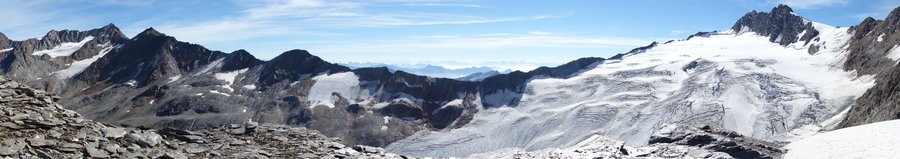 Der Panoramablick zeigt den letzten österreichischen Gebirgskamm vor der italienischen Grenze. Hier erstrecken sich die Eisflächen des Langtaler Ferners auf dieser Seite des Bergrückens nach Westen hinauf zum Annakogl, einem über dreitausenddreihundert Meter hohen Berggipfel. Außer dem azurblauen Himmel gibt es hier oben kaum Farben zu sehen. Der Fels erstrahlt in anthrazit-grauen Tönen, unterbrochen nur von weißen Schnee- und Eisflächen. Die Berge der italienischen Alpen im Hintergrund verblassen mit zunehmender Entfernung.